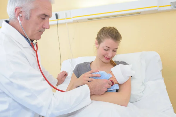Maduro macho médico examinar bebé chica con madre viendo —  Fotos de Stock