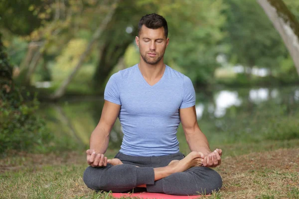 Man meditating outside by river — Stock Photo, Image