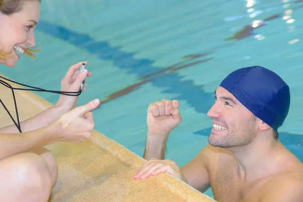 Χαμογελώντας εκπαιδευτής δείχνει το χρονόμετρο στο κολυμβητής στο κέντρο ελεύθερου χρόνου — Φωτογραφία Αρχείου