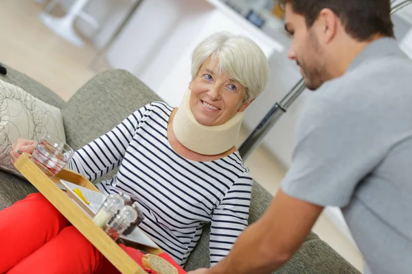 Sonriente anciana en sofá y enfermera sosteniendo bandeja — Foto de Stock