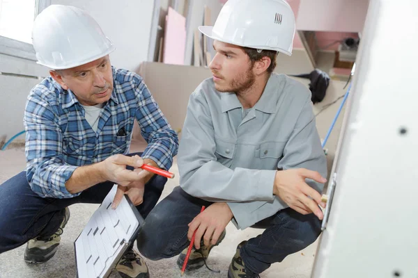 Dos constructores con portapapeles trabajando con electricidad en interiores —  Fotos de Stock