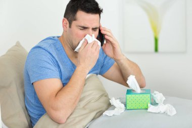 man coughing covering mouth with a tissue at home clipart