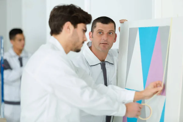 Aprendiz gravando papel de parede na parede — Fotografia de Stock