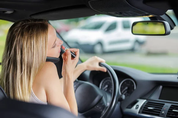 Conductor femenino hablando por teléfono celular y aplicando lápiz labial — Foto de Stock