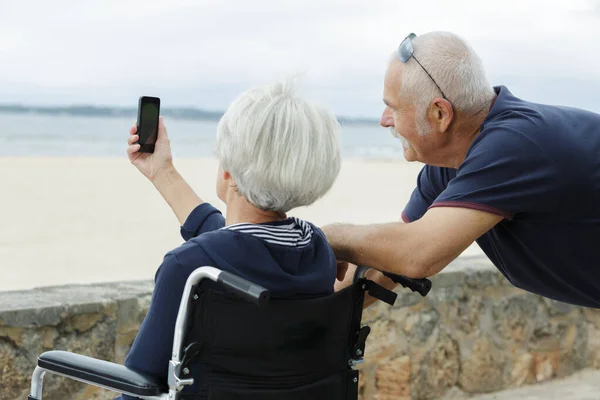 Пожилая пара в инвалидной коляске делает селфи — стоковое фото
