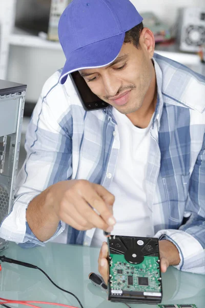Techniker am Telefon, der eine Festplatte repariert — Stockfoto