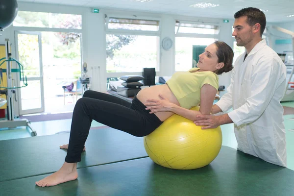 Läkare stöder gravida dam lutar sig tillbaka på en aerob boll — Stockfoto