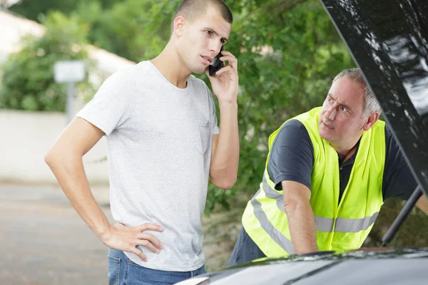 Молодой человек зовет на помощь, чтобы починить свой автомобиль — стоковое фото