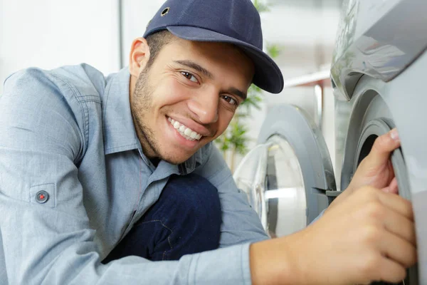 Working man plumber repairs a washing machine in laundry — Stock Photo, Image