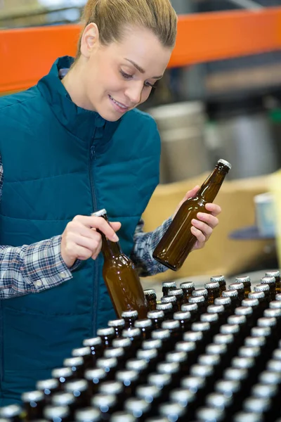 Joven trabajadora embotellando cerveza en botellas de vidrio en cervecería —  Fotos de Stock