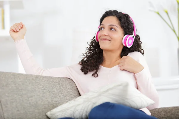 Розслаблена жінка з навушниками на дивані вдома слухає музику — стокове фото
