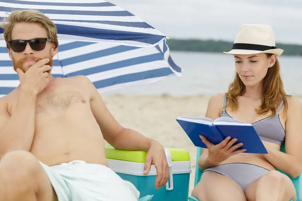 Par på stranden mannen ser uttråkad kvinna läser — Stockfoto