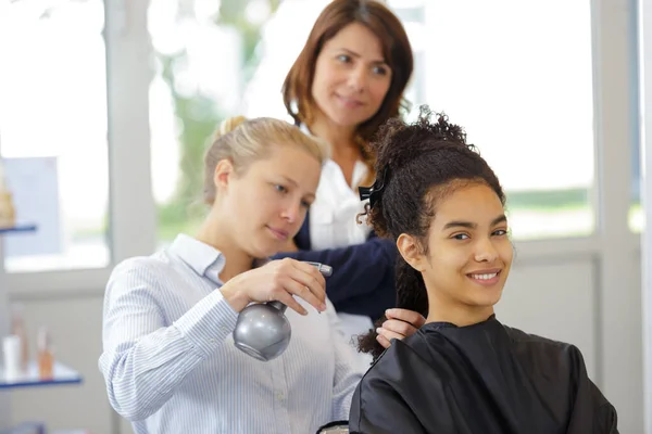 Kadeřnické učeň žehlit klientům vlasy — Stock fotografie
