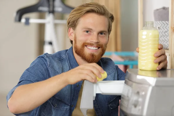 Jovem sorrindo derramando detergente líquido na máquina de lavar roupa — Fotografia de Stock