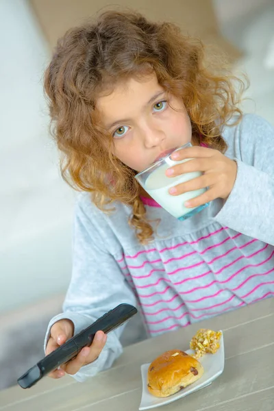 Niña sosteniendo vaso de leche y control remoto — Foto de Stock