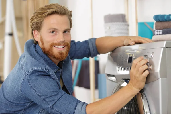 Homem carregando roupas na máquina de lavar roupa na cozinha — Fotografia de Stock