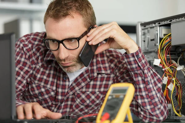 Reparador de computador falando no smartphone e usando laptop — Fotografia de Stock