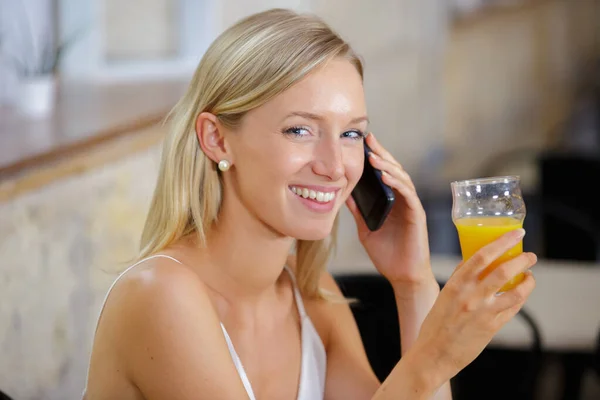 Молода жінка з апельсиновим соком і смартфоном — стокове фото