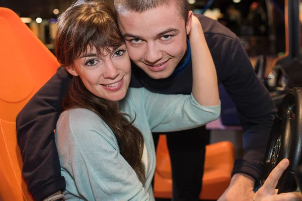 Portrait of young couple embracing at arcade driving game — Stock Photo, Image