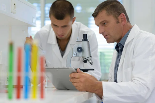 Dois cientistas do sexo masculino trabalhando em laboratório com microscópio e tablet — Fotografia de Stock