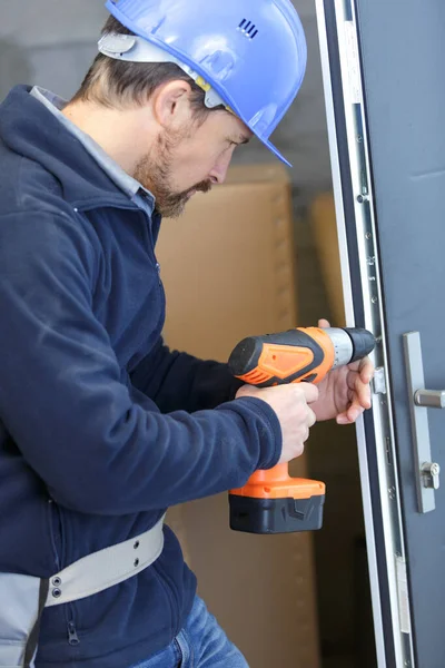 Mann mit Helm durchbohrt Wand mit Bohrer in den Händen — Stockfoto