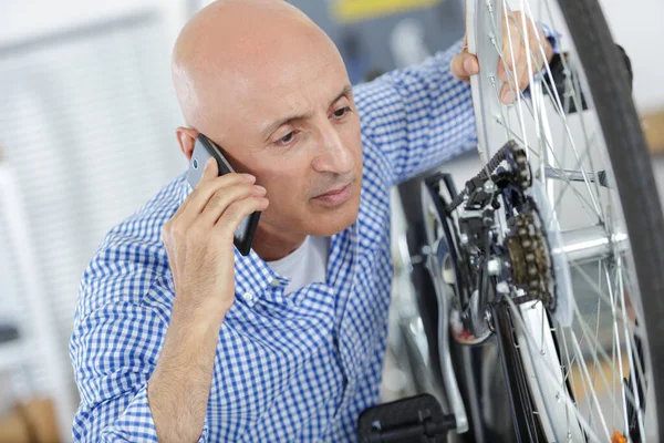 Homem falando no telefone celular durante a reparação de roda de bicicleta — Fotografia de Stock