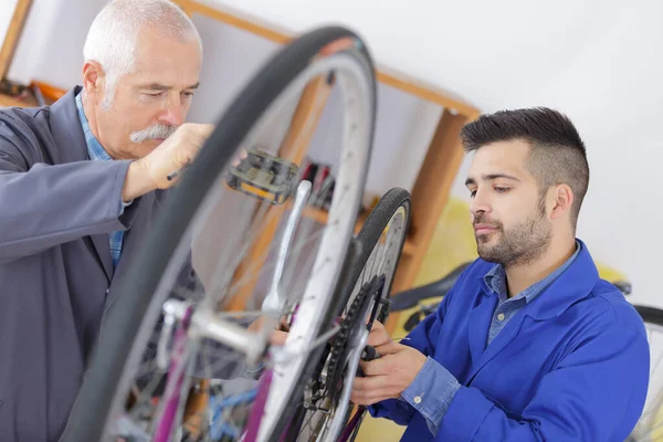 Vendedor homem sênior vestindo bicicleta de fixação uniforme na loja de esporte — Fotografia de Stock