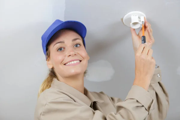 Female electrician mounting light fitting — Stockfoto