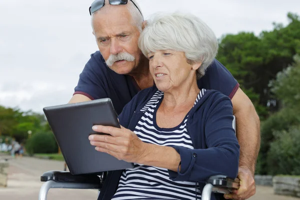 Starší pár pomocí tablet venku žena na invalidním vozíku — Stock fotografie