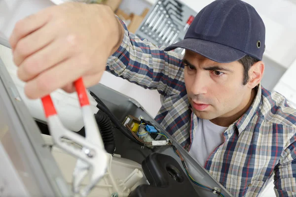 Homem trabalhador encanador repara uma máquina de lavar roupa — Fotografia de Stock