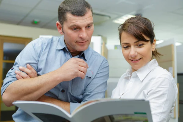 Sales assistant looking at catalogue with customer — Stockfoto