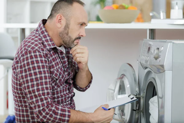 Plombier pensant avec presse-papiers près de la machine à laver — Photo