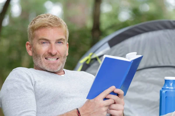 A man reading next to his tent — Stock Photo, Image