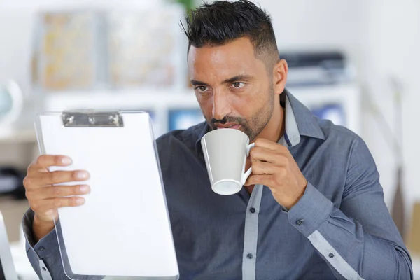 Homem de negócios barbudo verificando sua área de transferência enquanto bebe café — Fotografia de Stock