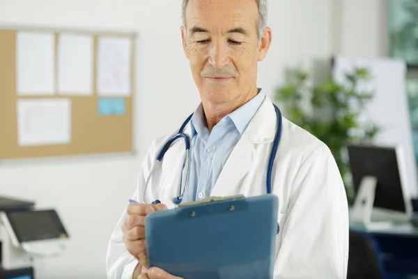 Senior man doctor in white uniform holding clipboard — ストック写真