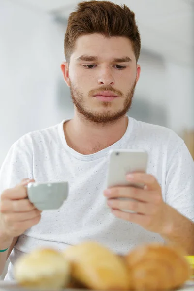 Mężczyzna cieszący się śniadaniem trzymając telefon — Zdjęcie stockowe