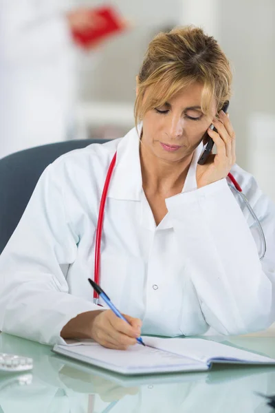 Orta yaşlı kadın doktor cep telefonuyla hastayla konuşuyor. — Stok fotoğraf