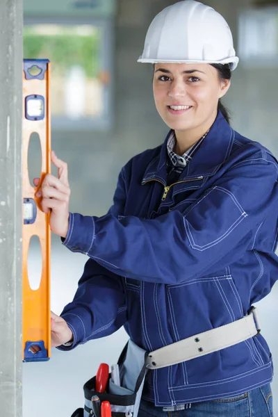 Mujer sonriente constructora en hardhat haciendo medidas con herramienta de nivel —  Fotos de Stock
