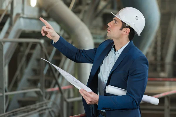 Handsome engineer pointing at pipes in a factory — Stockfoto