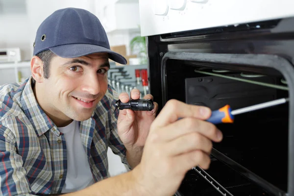 Repairman with screwdriver fixing oven in kitchen — Stock Photo, Image