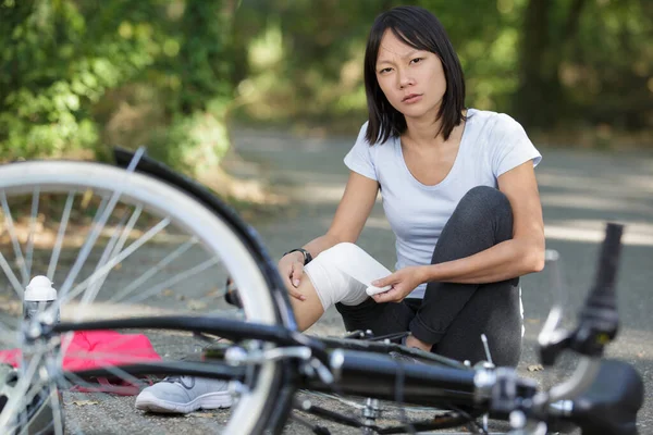 Mujer que aplica vendaje a la rodilla después de caer de la bicicleta — Foto de Stock