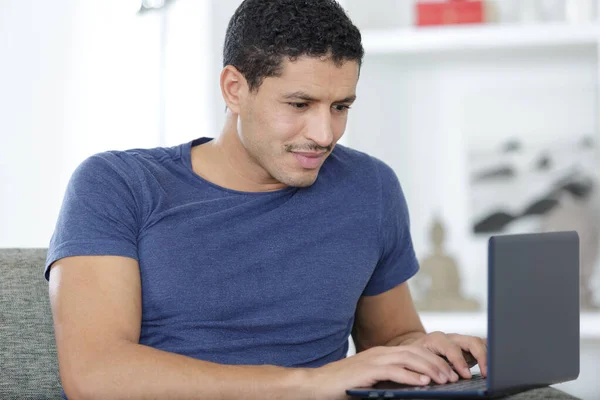 Hombre joven con el ordenador portátil en el sofá en casa —  Fotos de Stock