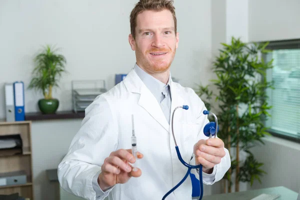 Męski lekarz trzymający strzykawkę i uśmiechający się do kamery — Zdjęcie stockowe