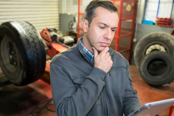 Mécanicien regardant presse-papiers dans le pneu dans le garage — Photo