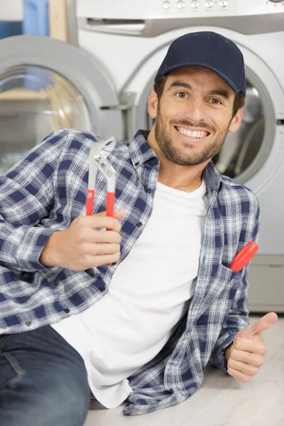 Reparador segurando uma chave ao lado de uma máquina de lavar roupa — Fotografia de Stock