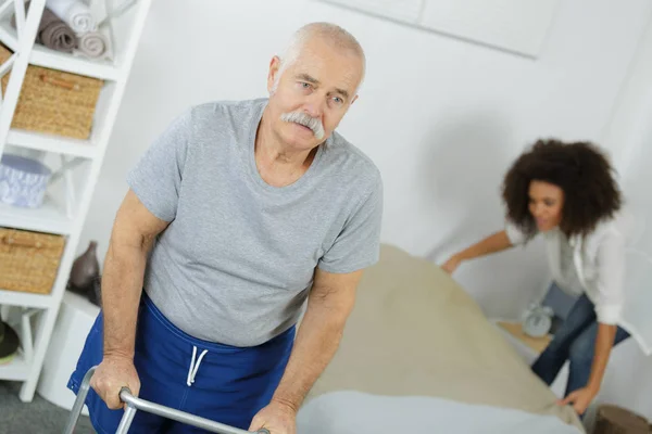 Starszy mężczyzna spacery z ramki whiler opiekun to ścielić łóżko — Zdjęcie stockowe