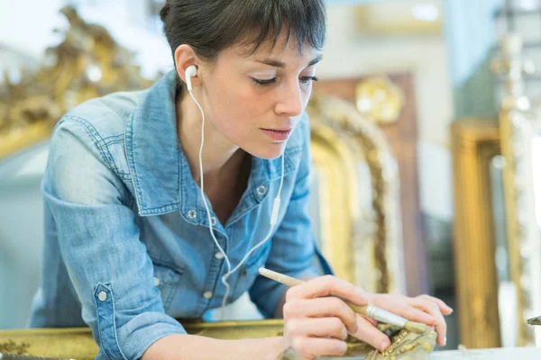Mujer que usa auriculares mientras restaura el marco dorado —  Fotos de Stock