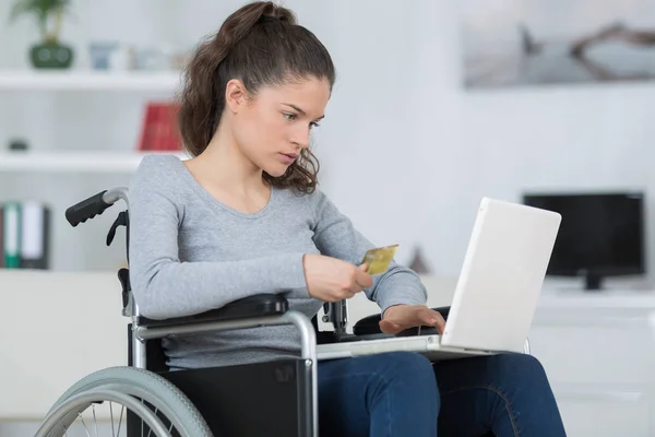 Kız tekerlekli sandalyede dizüstü bilgisayar kullanıyor ve banka kartı tutuyor. — Stok fotoğraf