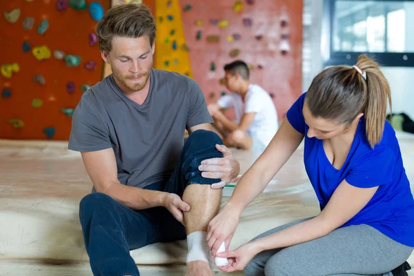 Mulher aplicando bandagem de compressão no homem lesão no tornozelo — Fotografia de Stock