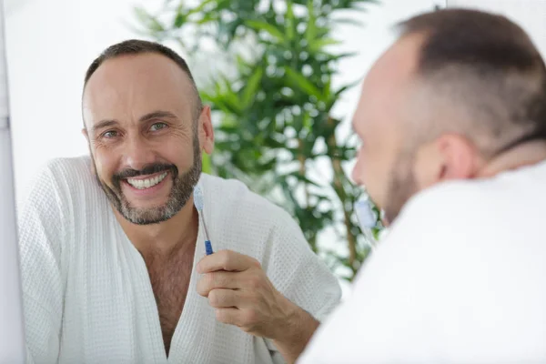 Bornoz giyen ve elinde diş fırçası tutan olgun bir adam. — Stok fotoğraf